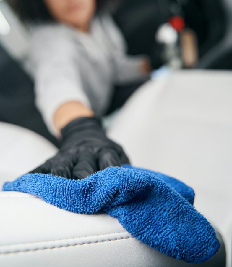 Gloved hand cleaning automotive leather upholstery using absorbent cloth