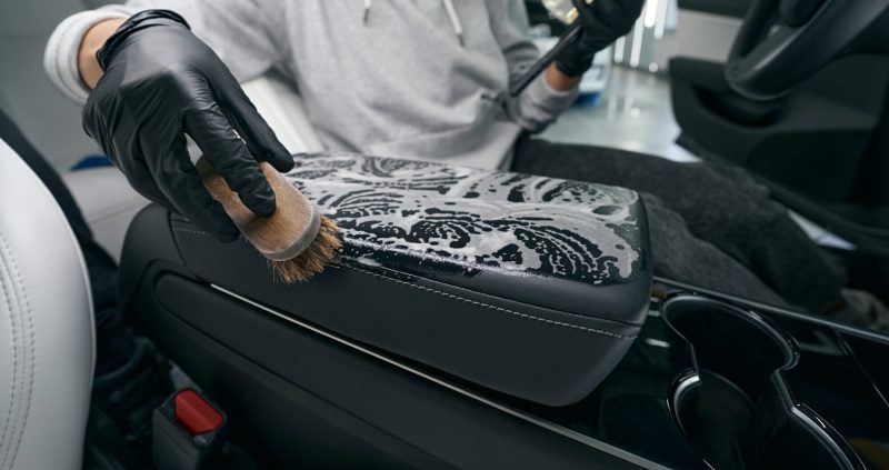 Worker using leather cleaner and brush for cleaning car upholstery